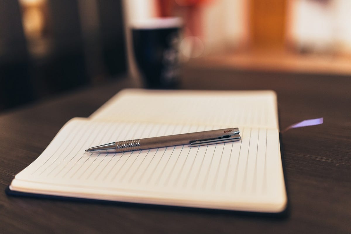 Open lined notebook with a silver pen resting on a dark wooden desk in warm indoor light